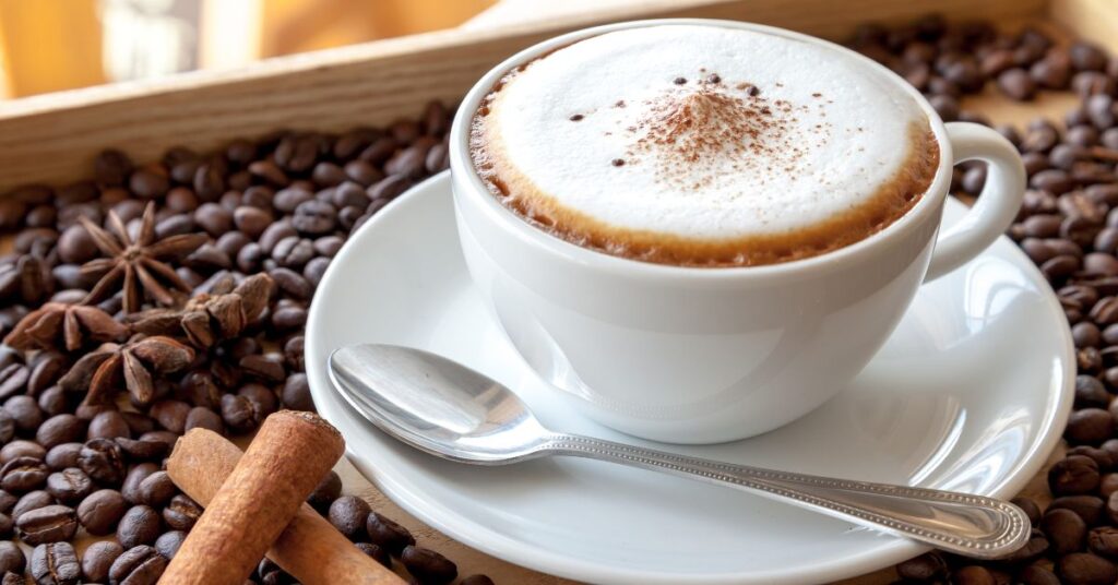 A Cappuccino with a teaspoon on the saucer and coffee beans around it